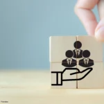 Holzwürfel mit stilisierten Personen symbolisieren Mitarbeiterfürsorge und Zusammenarbeit, passend zum Thema Gesundheitstag im Unternehmen planen und organisieren.