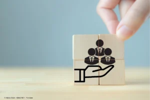 Holzwürfel mit stilisierten Personen symbolisieren Mitarbeiterfürsorge und Zusammenarbeit, passend zum Thema Gesundheitstag im Unternehmen planen und organisieren.